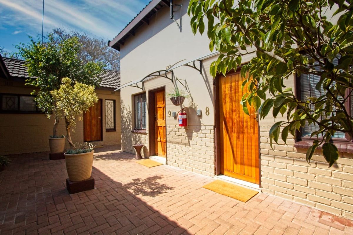 A well-maintained exterior courtyard area featuring brick paving, wooden entrance doors, and a covered walkway with a tiled roof.