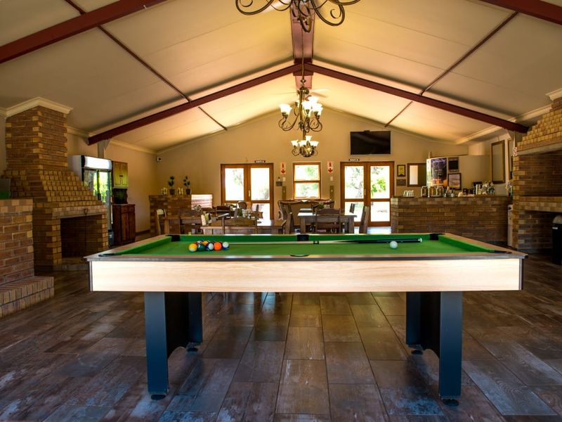 Spacious open-plan entertainment area featuring a vaulted ceiling with exposed beams, brick fireplace, built-in bar, and tiled flooring, ideal for social gatherings.