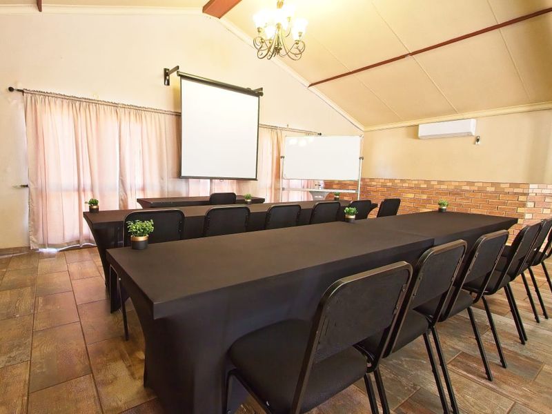 A functional utility space or conference room featuring vaulted ceilings, exposed brick accents, tiled flooring, and a wall-mounted projector screen.
