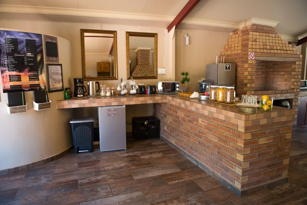 A rustic kitchen area featuring a prominent built-in brick fireplace, tiled countertops, and a brick breakfast bar with wood-look flooring.