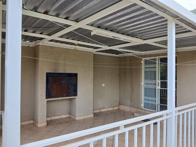 Covered patio area featuring a built-in braai, tiled flooring, and security gate access, offering a functional outdoor space in need of cosmetic maintenance.