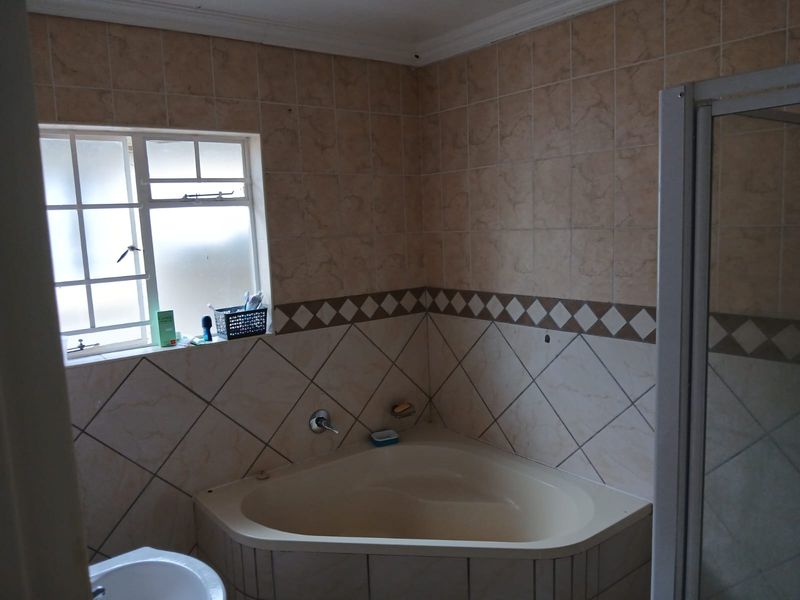 A dated bathroom featuring a corner bathtub, shower enclosure, and pedestal basin, finished with neutral wall tiling.
