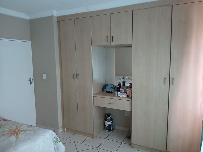 A bedroom featuring light wood-finish built-in cupboards with an integrated vanity area and tiled flooring.