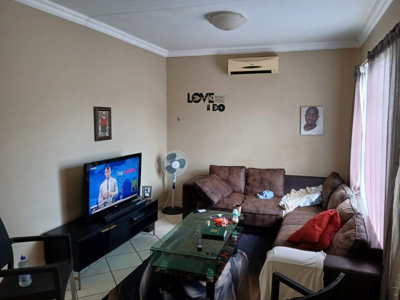 A living room featuring tiled flooring, a wall-mounted air conditioning unit, and decorative ceiling cornicing.