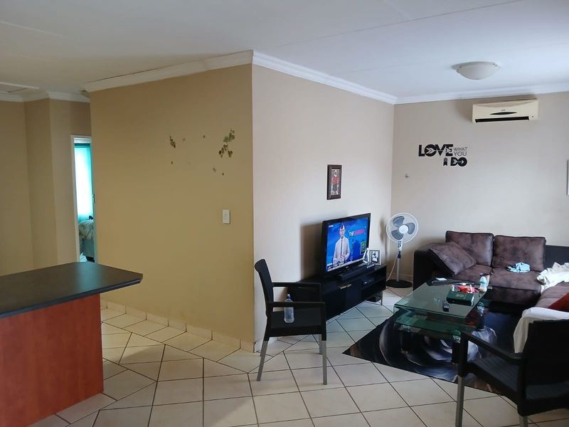 Open plan living area featuring tiled flooring, coving, and a wall-mounted air conditioning unit, connecting to the kitchen space.
