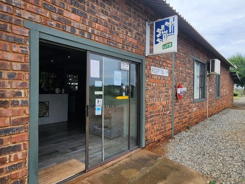 Exterior view of the guest house reception entrance featuring exposed brickwork, a sliding glass door, and clear signage.