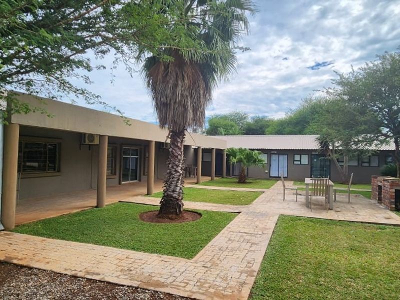 Spacious rear garden area featuring a covered patio, brick paved pathways, and a built-in brick braai, ideal for outdoor guest entertainment.