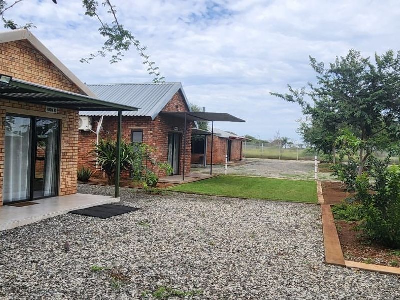 Exterior view of guest house units featuring face brick construction, covered patios, and well-maintained garden areas with gravel pathways.