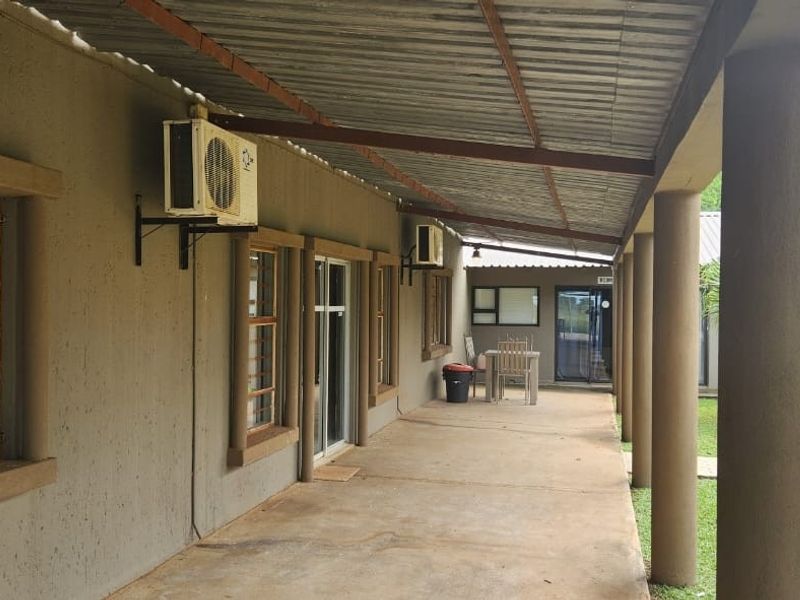 A covered outdoor patio area featuring concrete columns, corrugated roofing, and access to guest rooms via sliding glass doors.