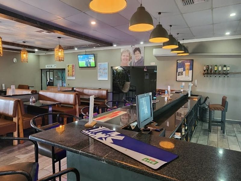 A well-maintained bar area featuring a long service counter, integrated display refrigeration, booth seating, and modern pendant lighting throughout the space.