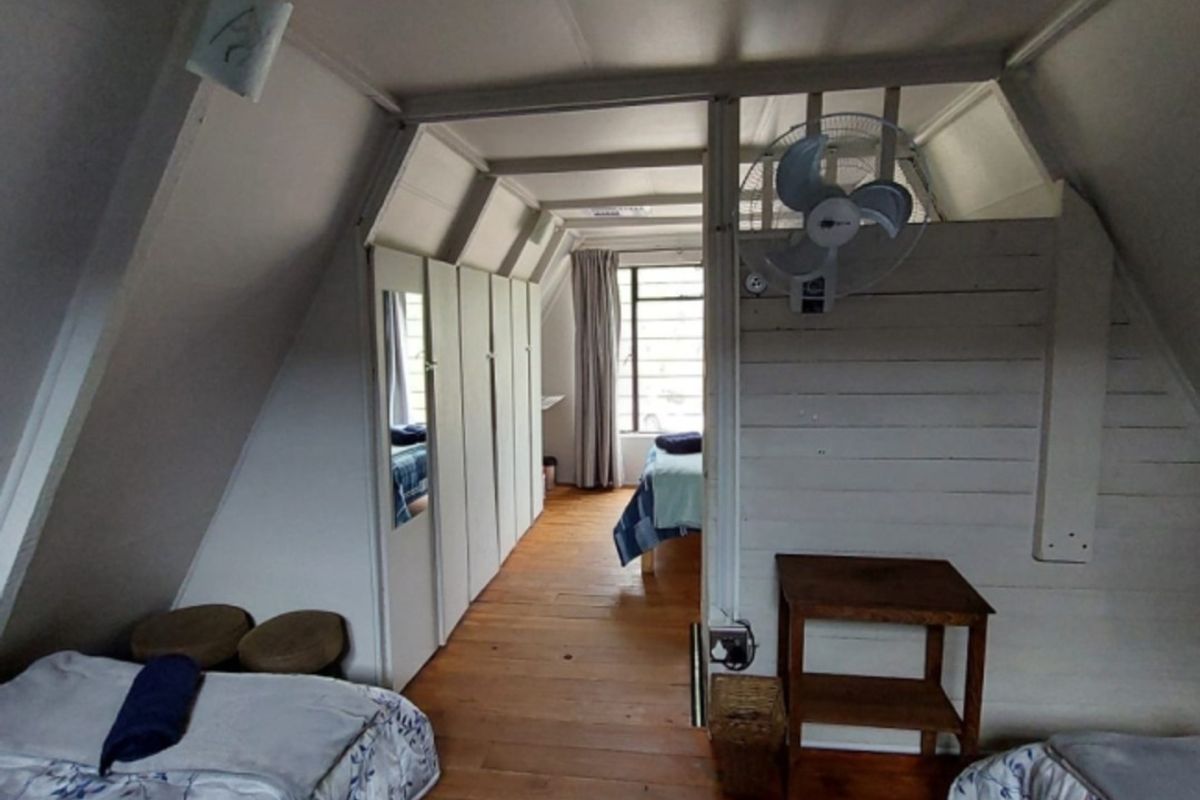 A rustic attic-style bedroom featuring timber flooring, sloped ceilings, and built-in storage cupboards.