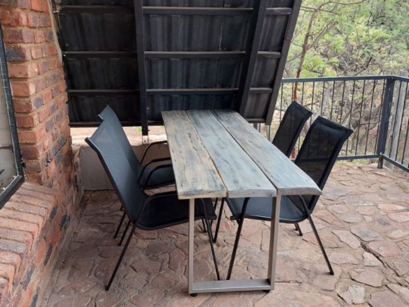 A covered outdoor patio area featuring exposed brickwork, stone paving, and a metal safety railing overlooking the surrounding landscape.
