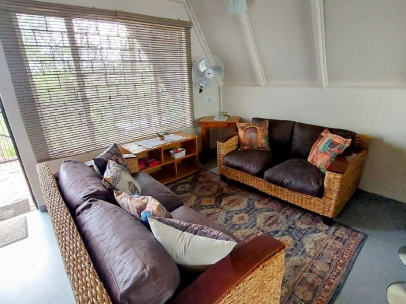 A cozy living room featuring a sloped ceiling with exposed rafters, large window with blinds, and neutral wall finishes.