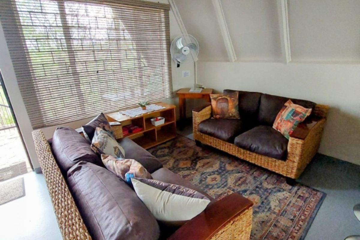A cozy living room featuring a sloped ceiling with exposed rafters, large window with blinds, and neutral wall finishes.