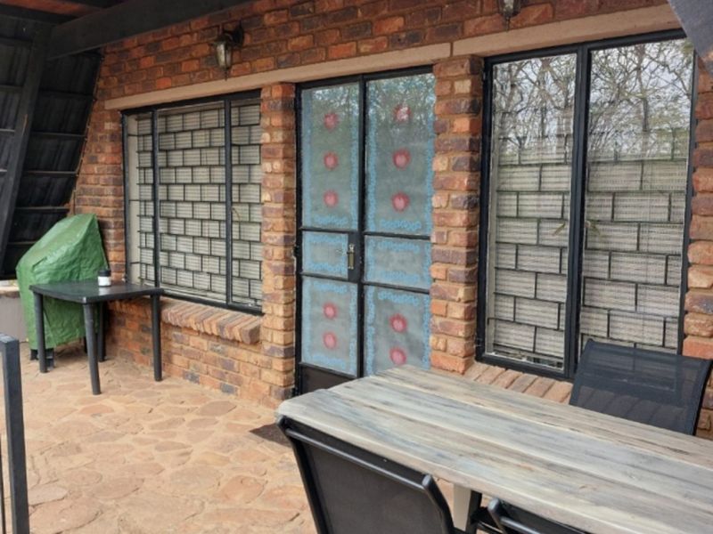 A covered patio area featuring exposed brick walls, stone flooring, timber beams, and secure metal window and door fixtures.
