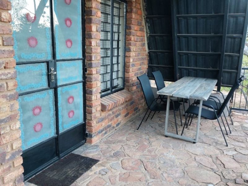 A rustic covered patio area featuring exposed brick walls, stone flooring, and a metal-framed glass entrance door, providing a functional outdoor space.