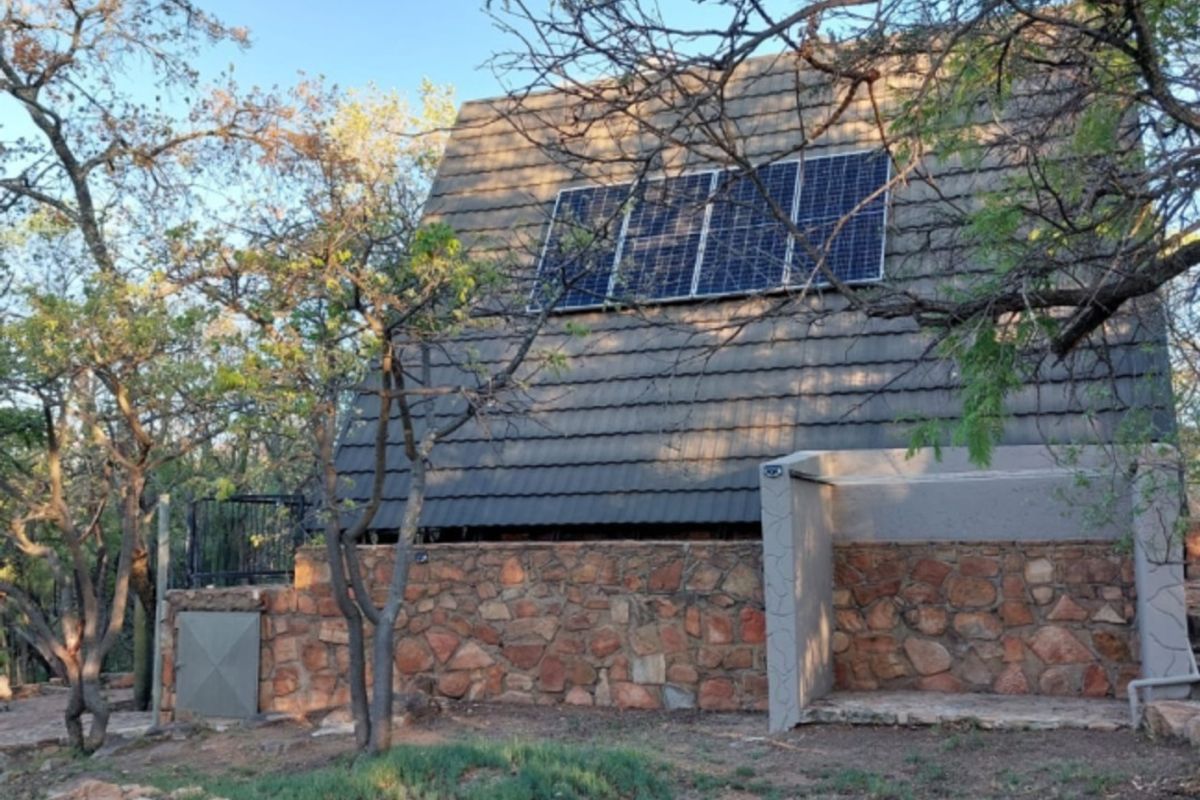 Rear view of the property featuring a pitched tiled roof with integrated solar panels and natural stone wall cladding.