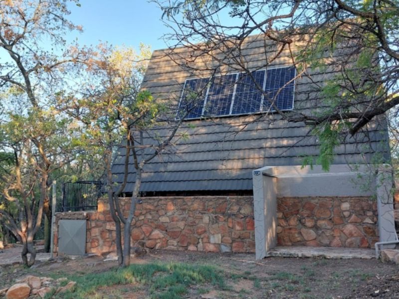 Rear view of the property featuring a pitched tiled roof with integrated solar panels and natural stone wall cladding.