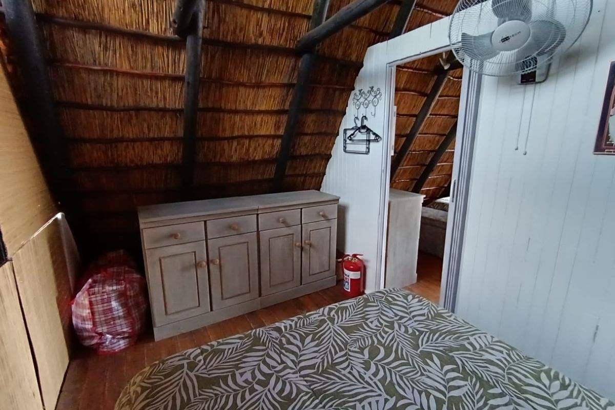 Bedroom featuring a traditional thatched roof with exposed timber rafters, timber flooring, and a wall-mounted fan.