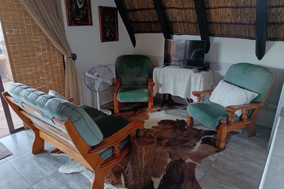 A cozy living area featuring a traditional thatched roof with exposed timber rafters and neutral tiled flooring.