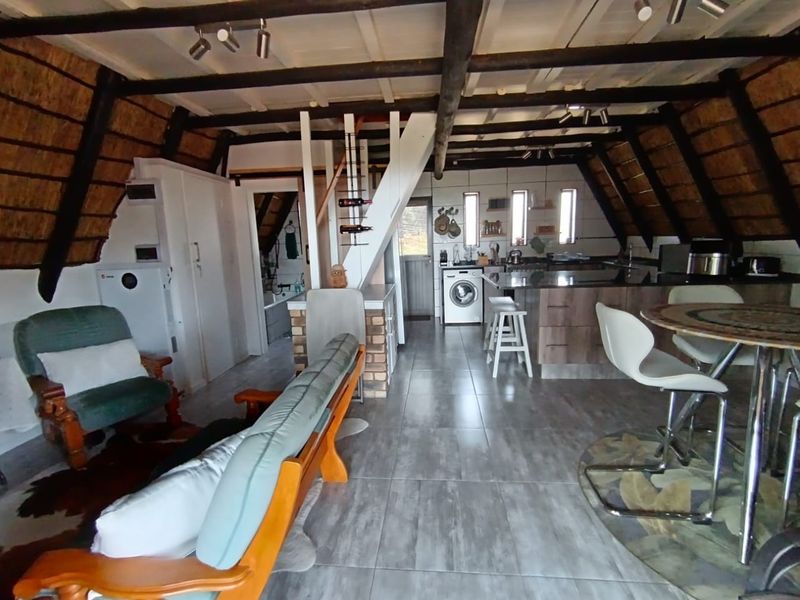Open-plan living and kitchen area featuring exposed timber rafters, thatched ceiling, tiled flooring, and a central kitchen island with built-in cabinetry.