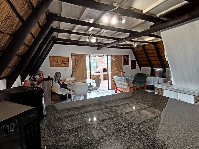 Open-plan living area featuring exposed timber beams, a thatched ceiling, and a granite kitchen island, with direct access to an outdoor patio area.