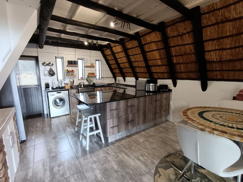 Open-plan kitchen featuring a central island with granite countertops, exposed timber beams, and a unique thatched roof ceiling design.
