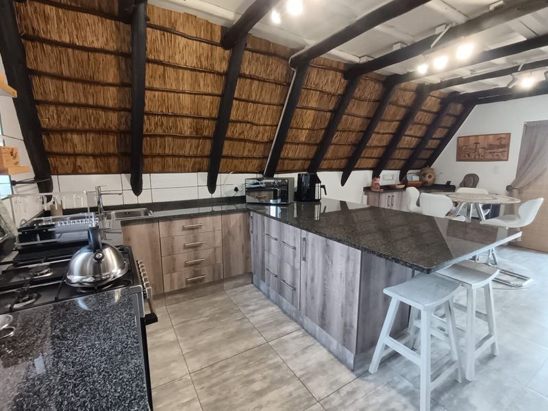 Modern kitchen featuring granite countertops, a central island, and gas stove, set under a unique vaulted thatched ceiling with exposed timber rafters.