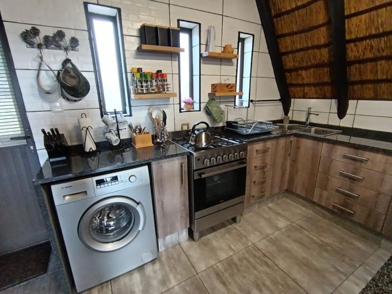 A functional kitchen featuring granite countertops, a gas stove, built-in cabinetry, and a tiled backsplash, set under a unique thatched roof structure.
