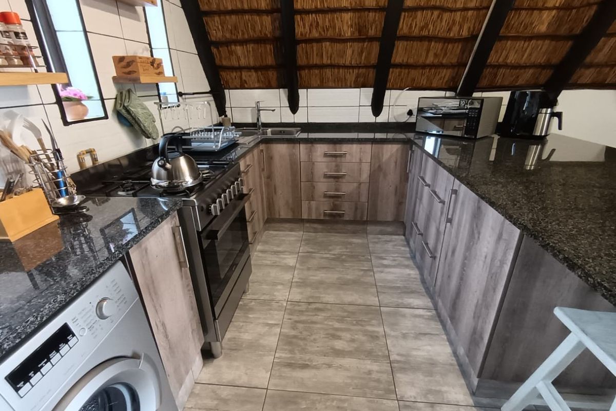 Modern kitchen featuring granite countertops, wood-finish cabinetry, gas stove, and unique exposed thatch roof detailing, providing a functional and stylish cooking space.