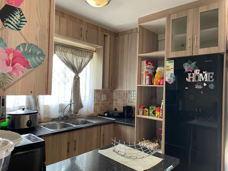 A functional kitchen featuring wood-look laminate cabinetry, a double bowl stainless steel sink, tiled backsplash, and integrated shelving for storage.