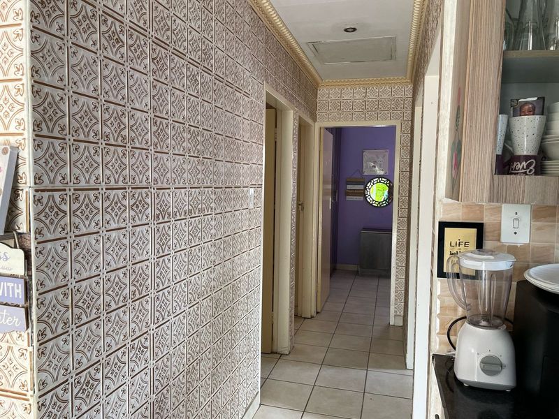 A functional hallway featuring decorative wall tiles, ceramic floor tiling, and ceiling cornice detailing, providing access to adjacent rooms.
