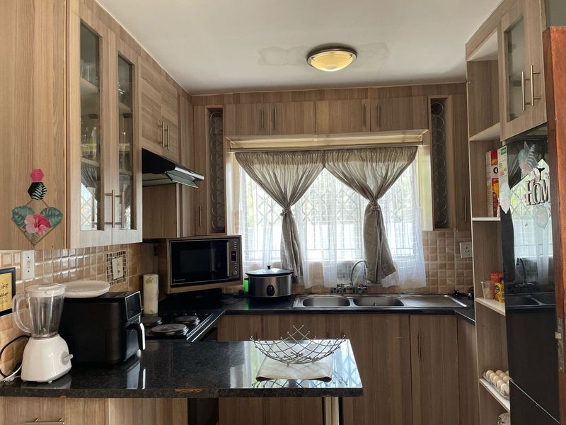 A functional kitchen featuring wood-look cabinetry, dark laminate countertops, a double basin sink, and integrated hob with extractor fan.