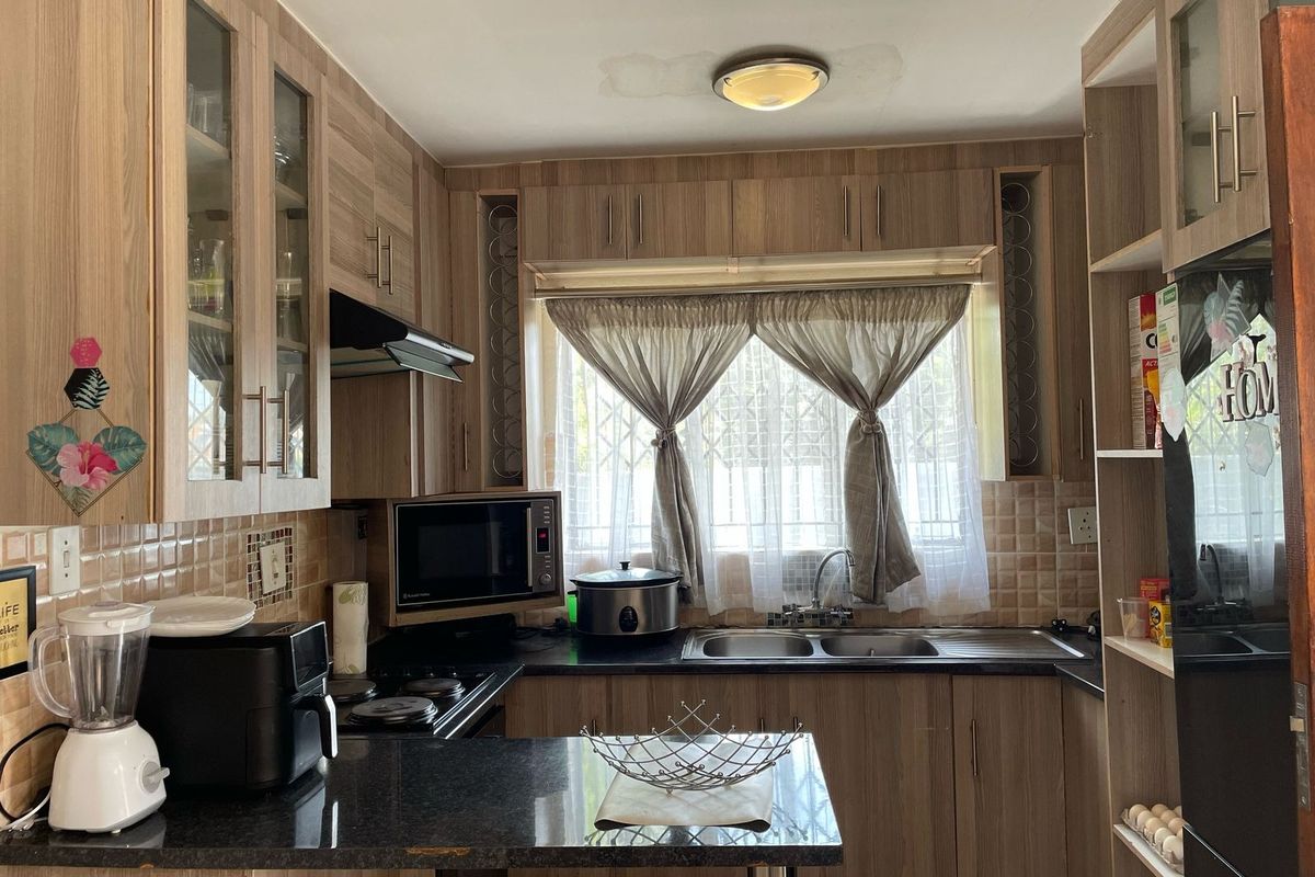 A functional kitchen featuring wood-look cabinetry, dark laminate countertops, a double basin sink, and integrated hob with extractor fan.