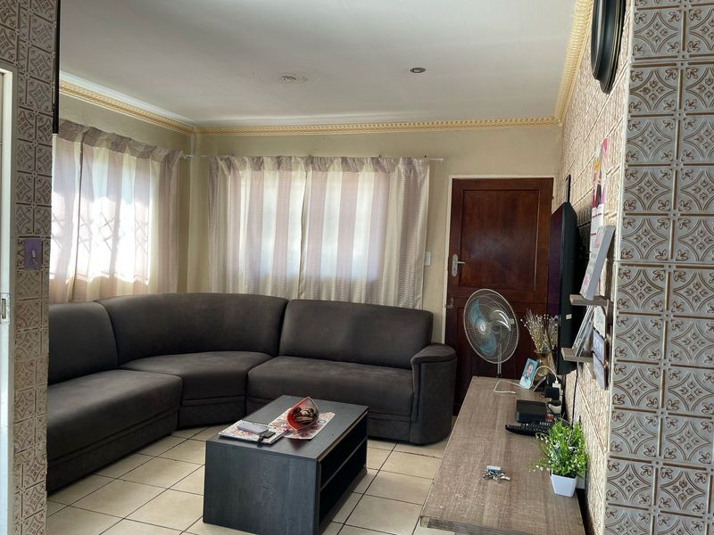 A living room featuring tiled flooring, decorative ceiling cornicing, and distinctive patterned wall tiles, providing a functional and lived-in space.