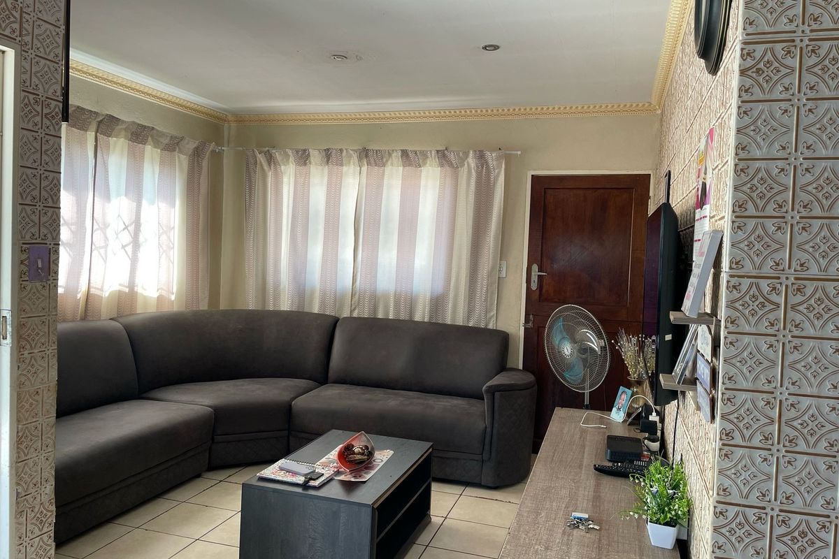 A living room featuring tiled flooring, decorative ceiling cornicing, and distinctive patterned wall tiles, providing a functional and lived-in space.