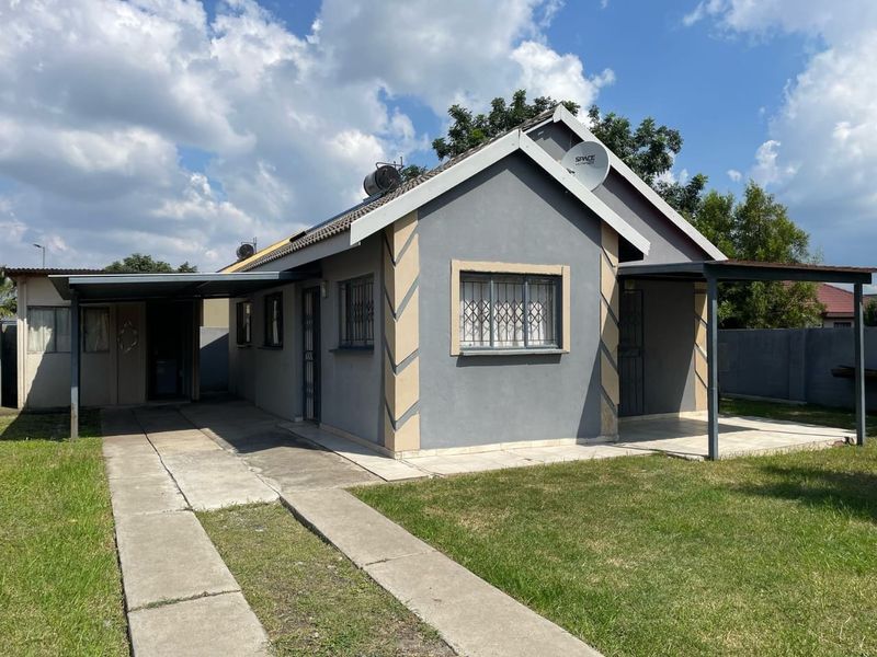Front view of a single-story house featuring a carport, concrete driveway, security bars on windows, and a small covered patio area.