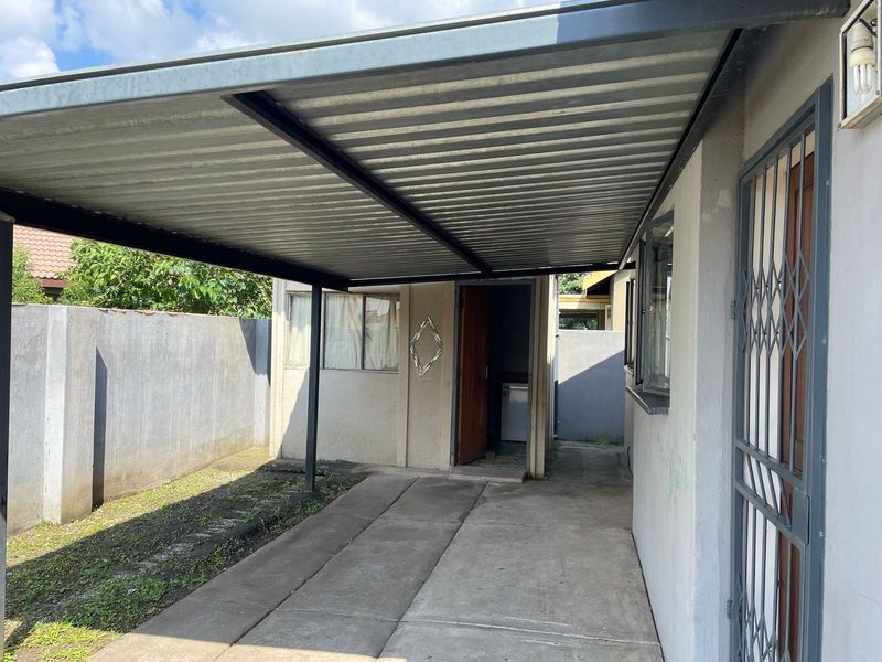 A covered outdoor patio area featuring a corrugated metal roof, concrete paving, and secure access points, suitable for outdoor living or storage.