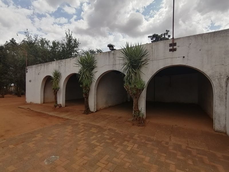 A multi-bay open garage structure featuring arched openings and a paved driveway area, showing signs of weathered exterior finishes.