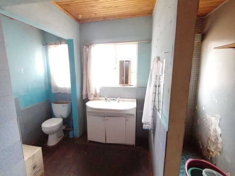 A dated bathroom featuring a vanity unit, toilet, and timber ceiling, currently requiring significant cosmetic renovation and wall repairs.