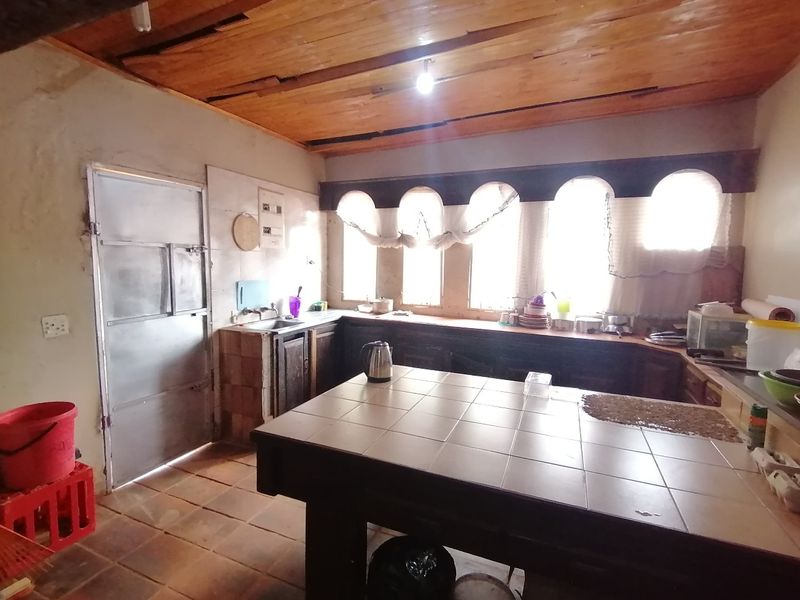 A dated kitchen featuring a tiled island, timber ceiling, and arched windows, requiring renovation to modernize the finishes and improve overall condition.