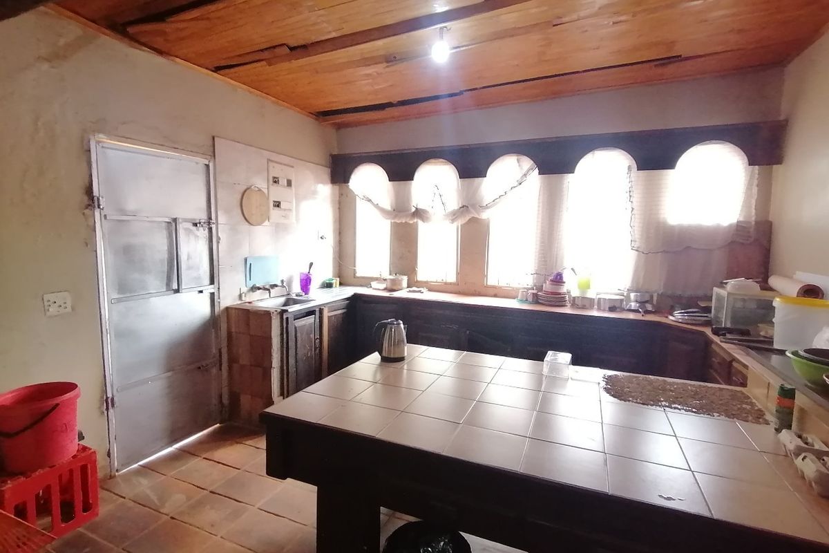 A dated kitchen featuring a tiled island, timber ceiling, and arched windows, requiring renovation to modernize the finishes and improve overall condition.