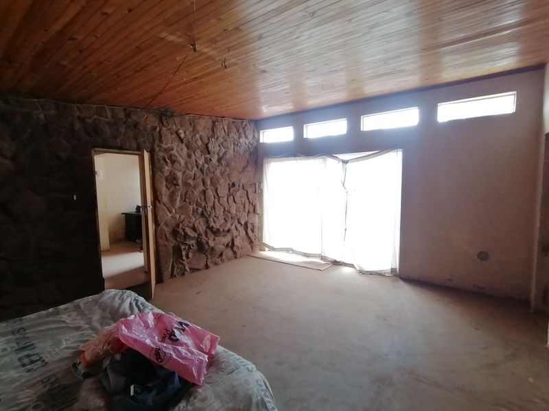 Spacious bedroom featuring a rustic stone feature wall, timber ceiling, and clerestory windows, offering a unique architectural foundation for renovation.