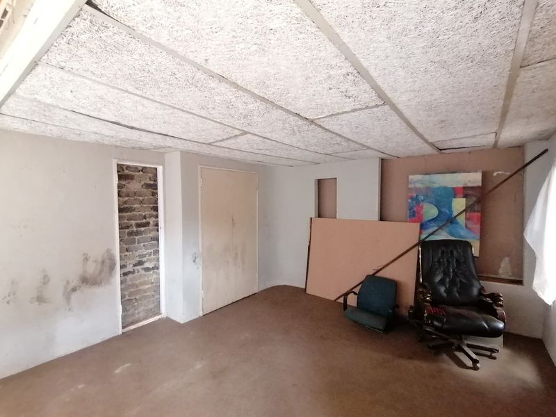 A bedroom space requiring significant renovation, featuring acoustic ceiling tiles, built-in storage, and unfinished wall surfaces.