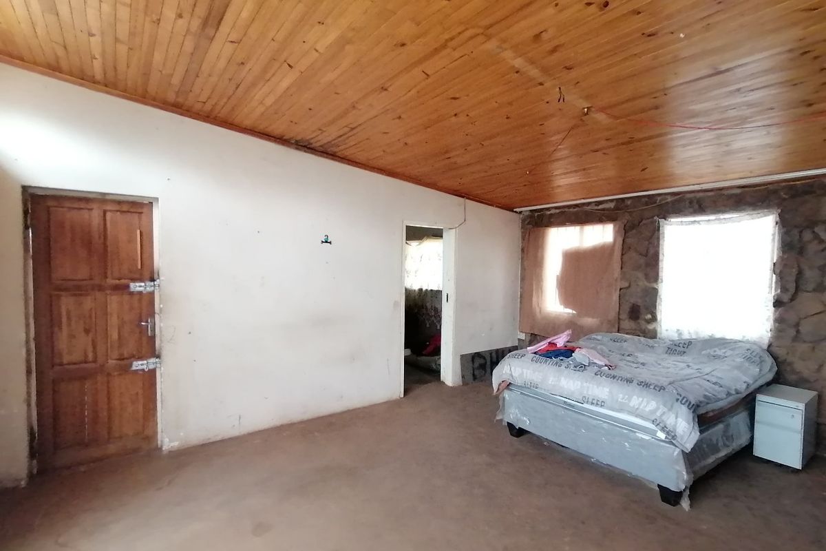 A bedroom featuring a timber ceiling and a rustic stone feature wall, requiring cosmetic updates to the flooring and wall finishes.