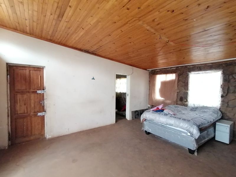 A bedroom featuring a timber ceiling and a rustic stone feature wall, requiring cosmetic updates to the flooring and wall finishes.