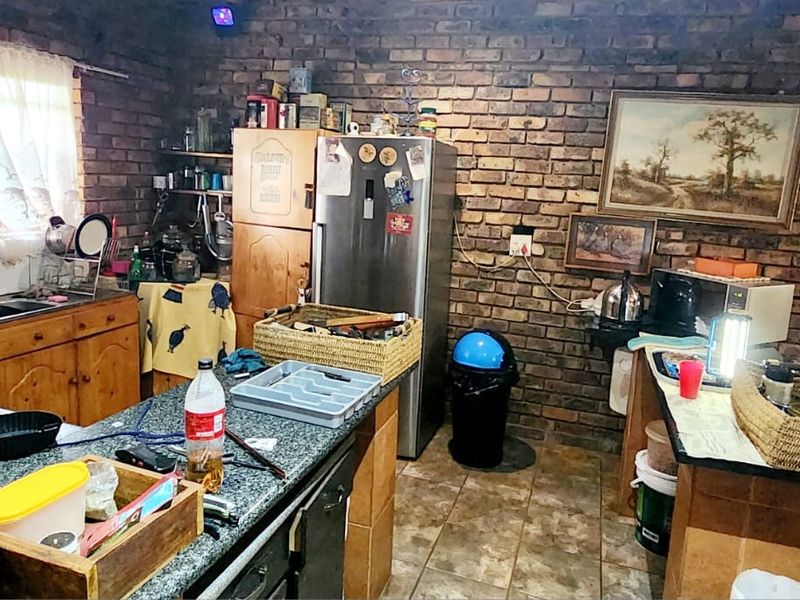 A rustic kitchen featuring exposed brick walls, tiled flooring, and wooden cabinetry with laminate countertops, offering a traditional farm-style aesthetic.