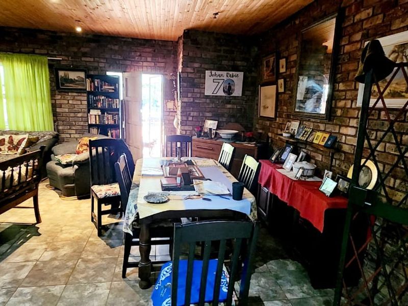 Open plan living and dining area featuring rustic exposed brick walls, timber ceiling, and tiled flooring, creating a warm and traditional farm-style atmosphere.