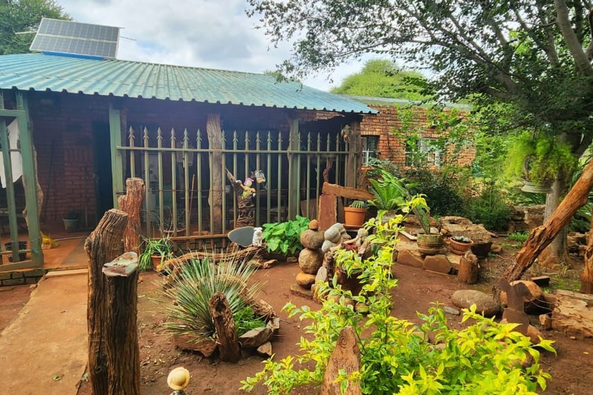 Rear view of a brick farm dwelling featuring a corrugated metal roof with a solar panel and surrounding garden area with security fencing.