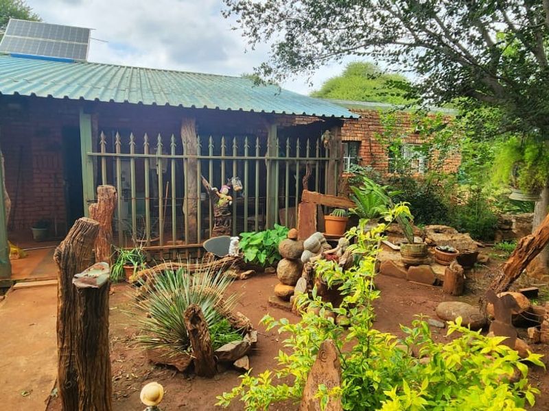 Rear view of a brick farm dwelling featuring a corrugated metal roof with a solar panel and surrounding garden area with security fencing.
